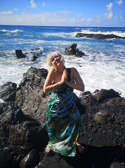 Eine Frau faltet die Hände zur Dankbarkeit auf einem Felsen vor dem Meer